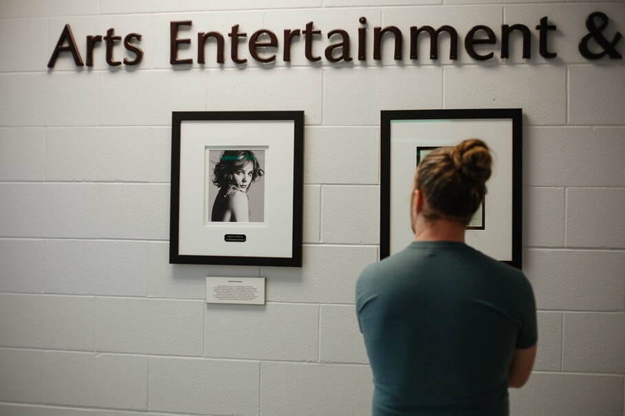 man looks at a framed image of Racehl McAdams on the wall under the heading Arts & Entertainment